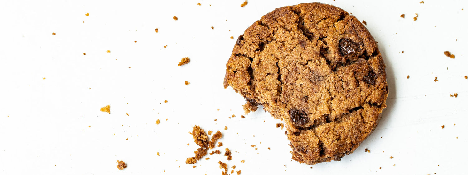 a chocolate chip cookie on a white background with a bite taken out of it and crumbs scattered around
