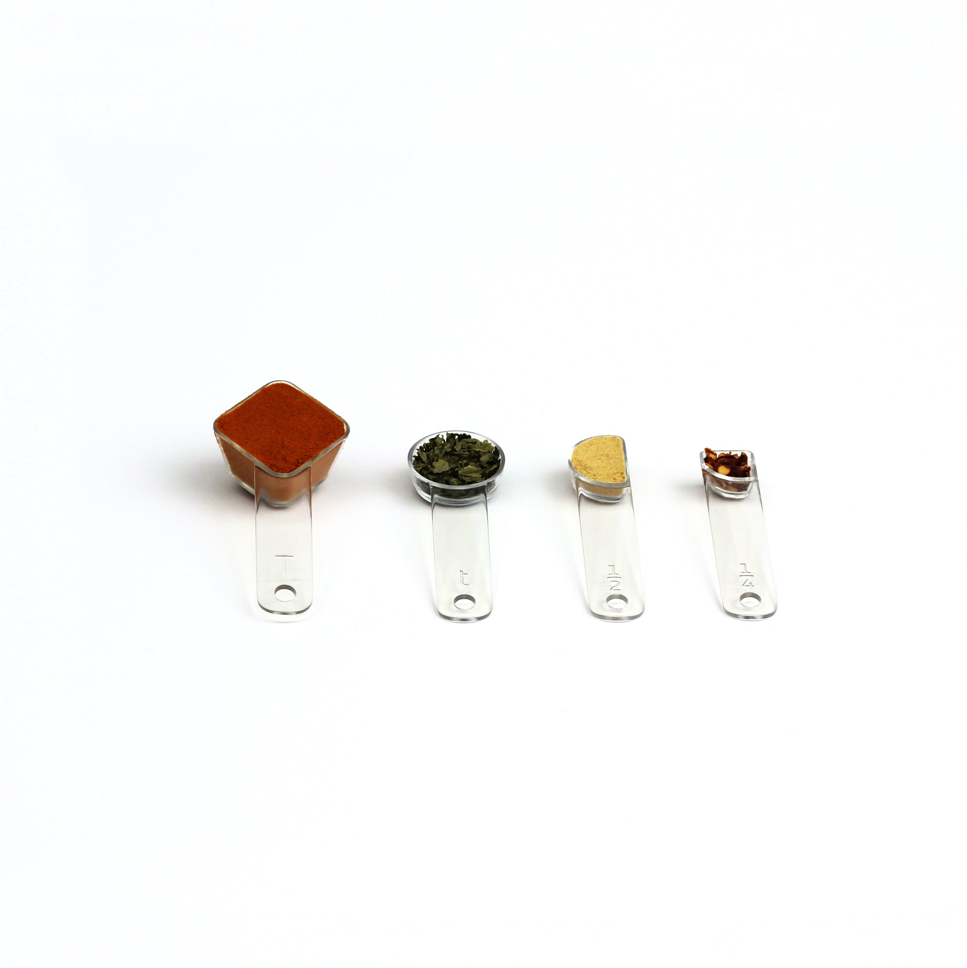 four visual measuring spoons, each a different shape to show the size, are arrayed with colorful spices