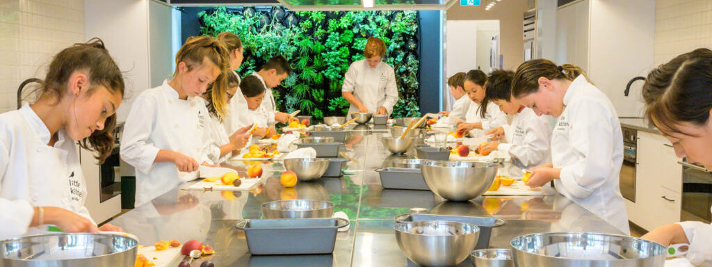 a large stainless steel kitchen area with young chefs along each side