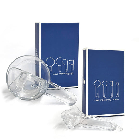 a set of nested clear visual measuring cups and spoons rest on their  side in front of their blue box packaging